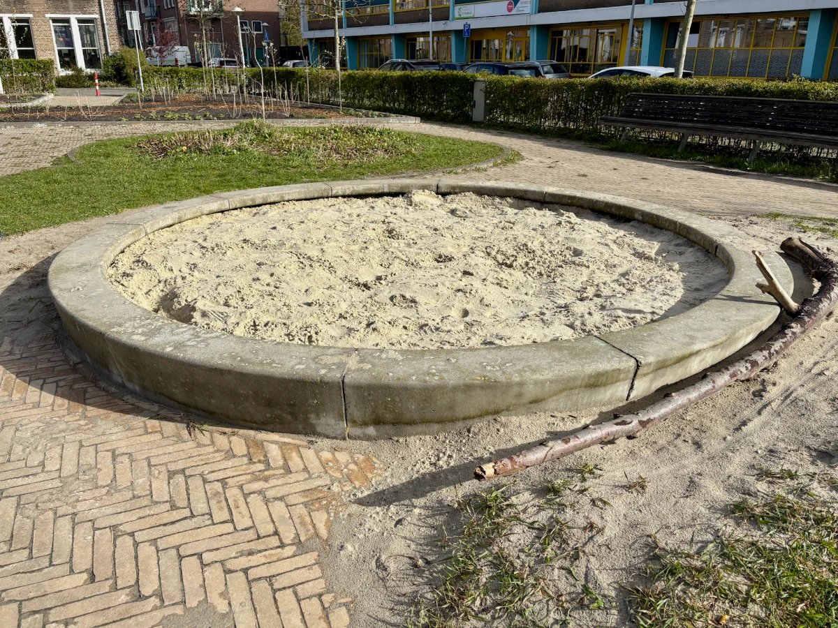 Circular concrete sand box with grassy area and brick pavers around it