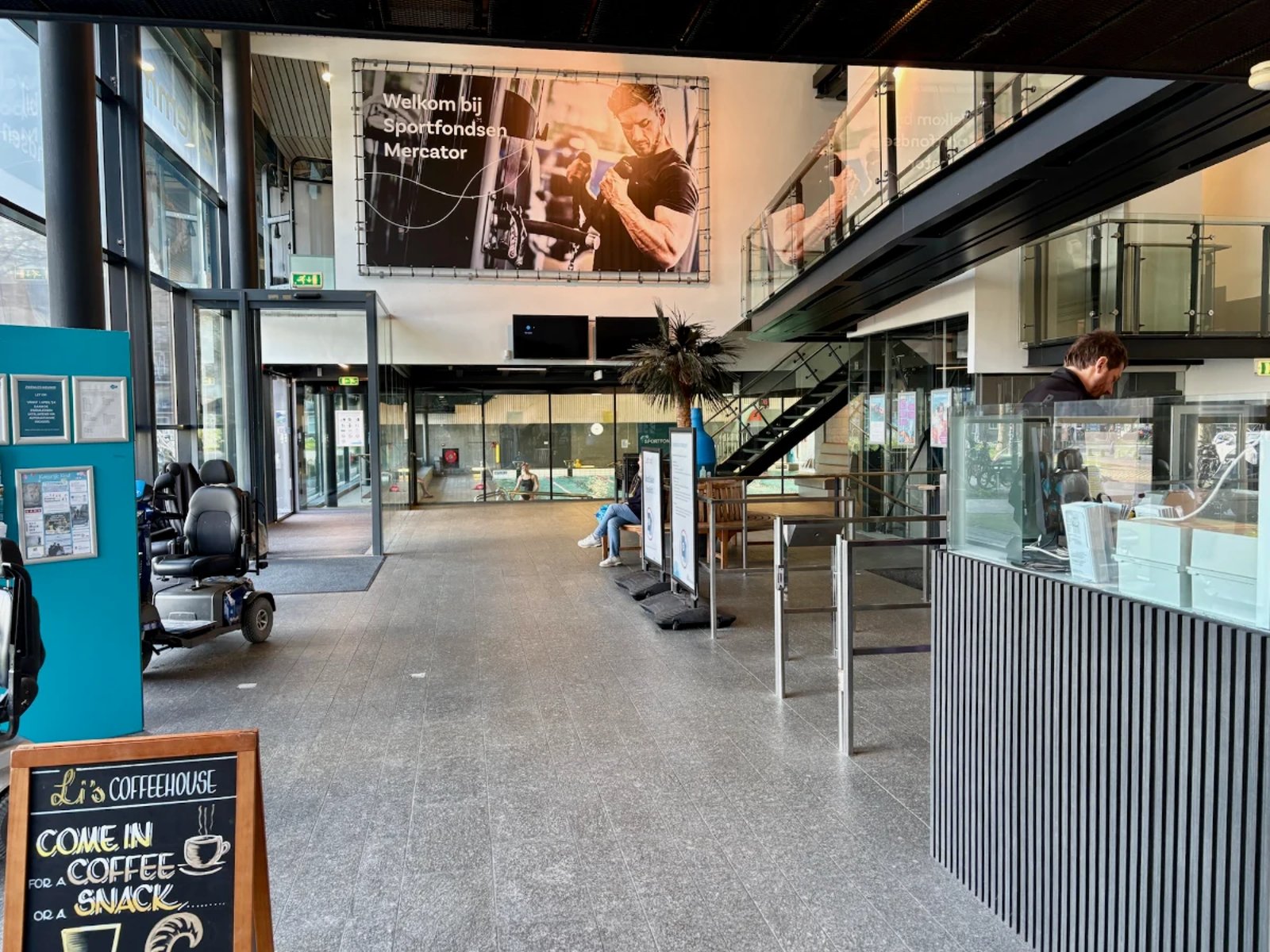 Entrance and check in counter with pool visible behind glass and large photo on the wall of a man lifting weights