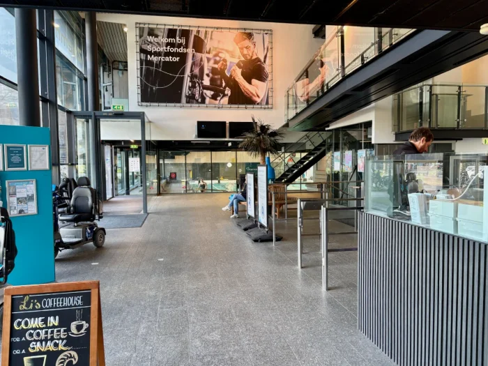 Entrance and check in counter with pool visible behind glass and large photo on the wall of a man lifting weights