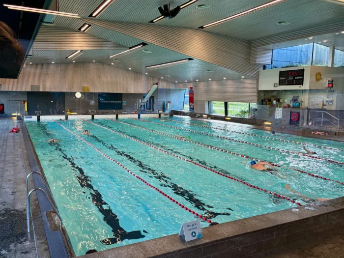 People swimming laps in pool with 6 lanes in modern facility with angled wood-slatted ceiling