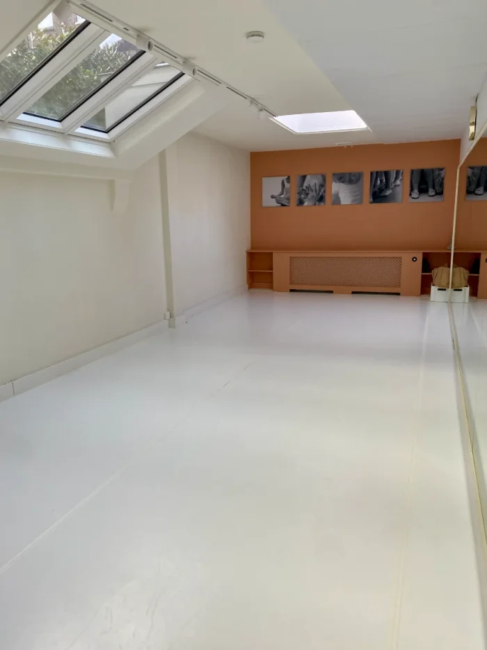Dance studio with white walls and floors, skylights, and orange accent wall with black and white photos of dancers