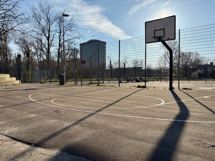 Expansive outdoor basketball court with hoop in foreground and other courts and people playing far in the distance