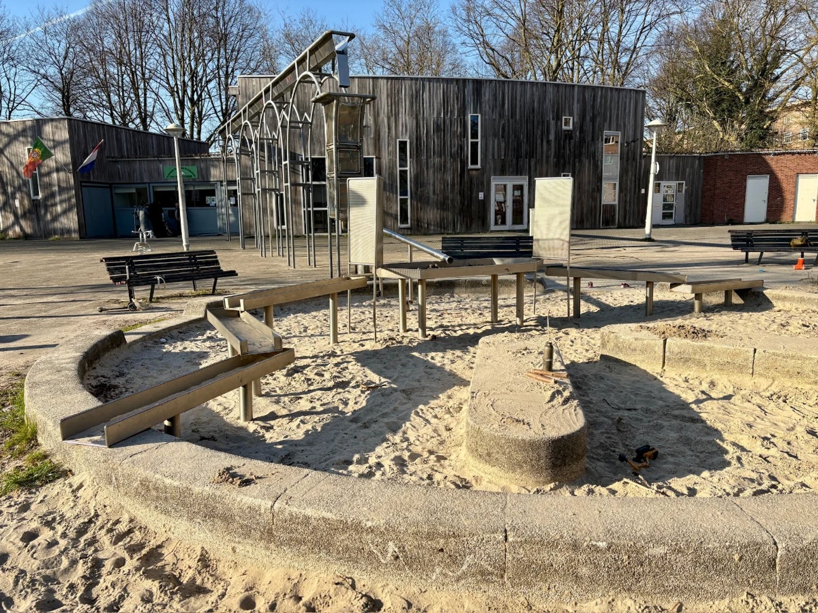 Round sand box with metal channel for water play with wooden building and metal ornate trellis structure in the background