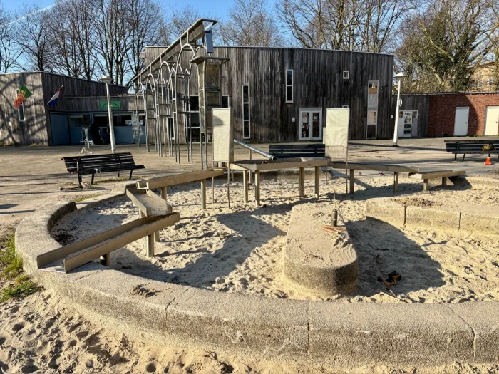 Round sand box with metal channel for water play with wooden building and metal ornate trellis structure in the background