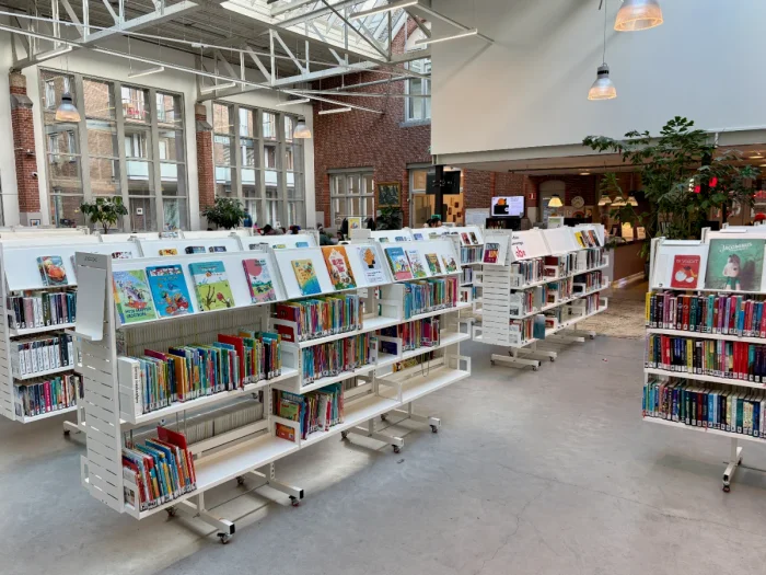 Rows of white bookcases with colorful books in a bright, airy converted warehouse space