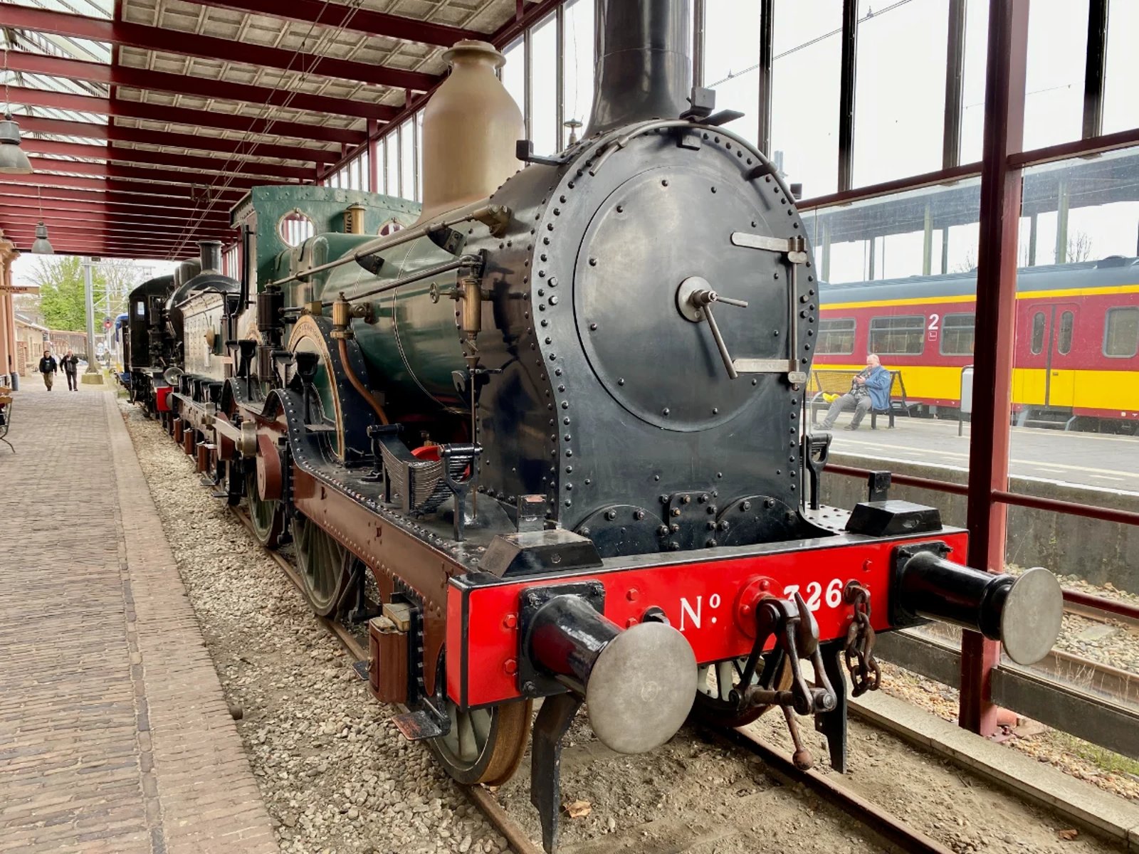 Vintage black, green, and red steam engine along a covered station platform