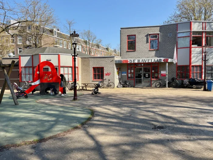 Red and grey community center building with red play structure and slide in the foreground