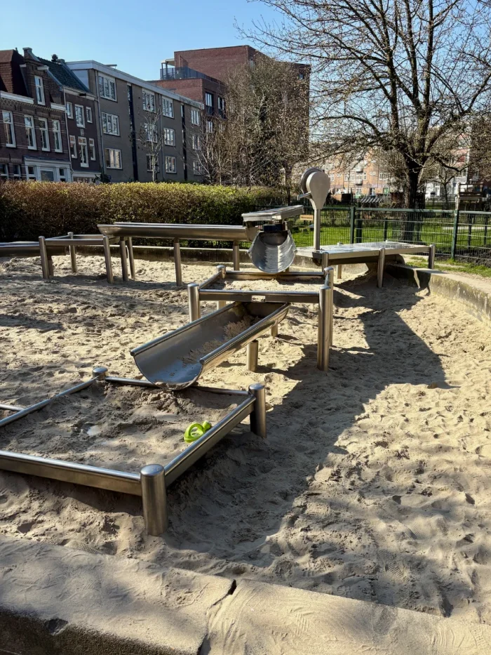 Large sand box with water channels for sand/water play surrounded by residential buildings and trees