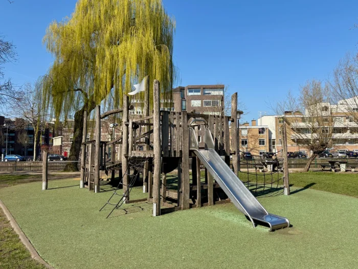 Wooden play structure with climbing nets and slide on green grass with spring tree and blue skies behind