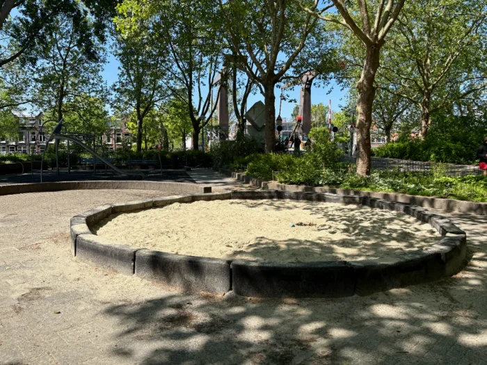 Round, partially shaded sandbox with large trees around