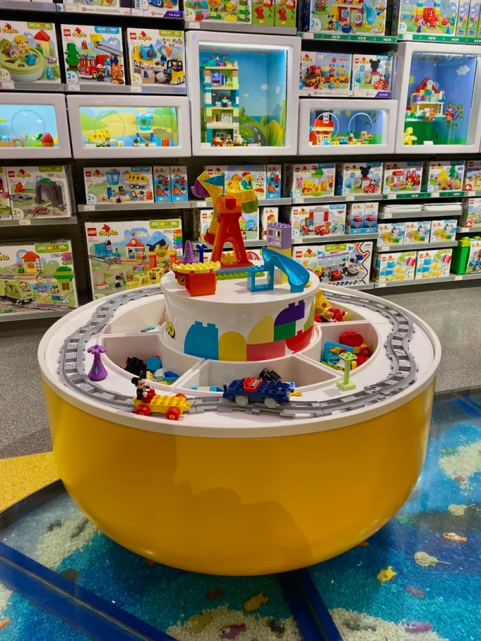 Round build-your-own station with train tracks and vehicles with LEGO merchandise on shelves