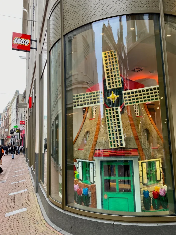 LEGO store entrance with red sign outside and large LEGO-built windmill on display in the storefront