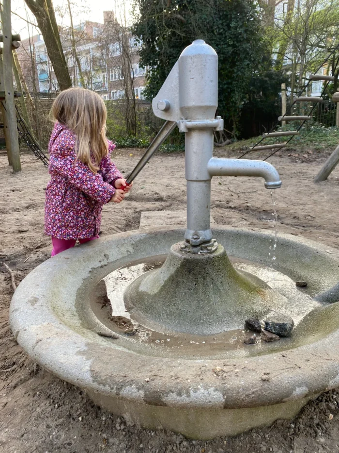 Girl in pink coat pumping water into a basin