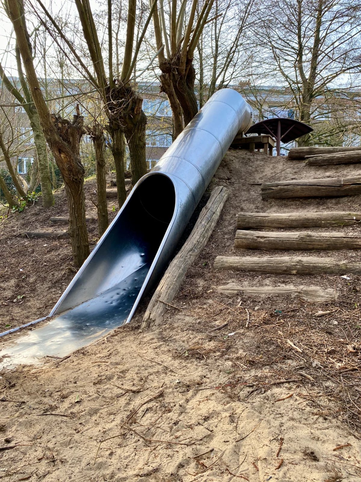 Metal slide set into a hillside with logs forming stairs to either side
