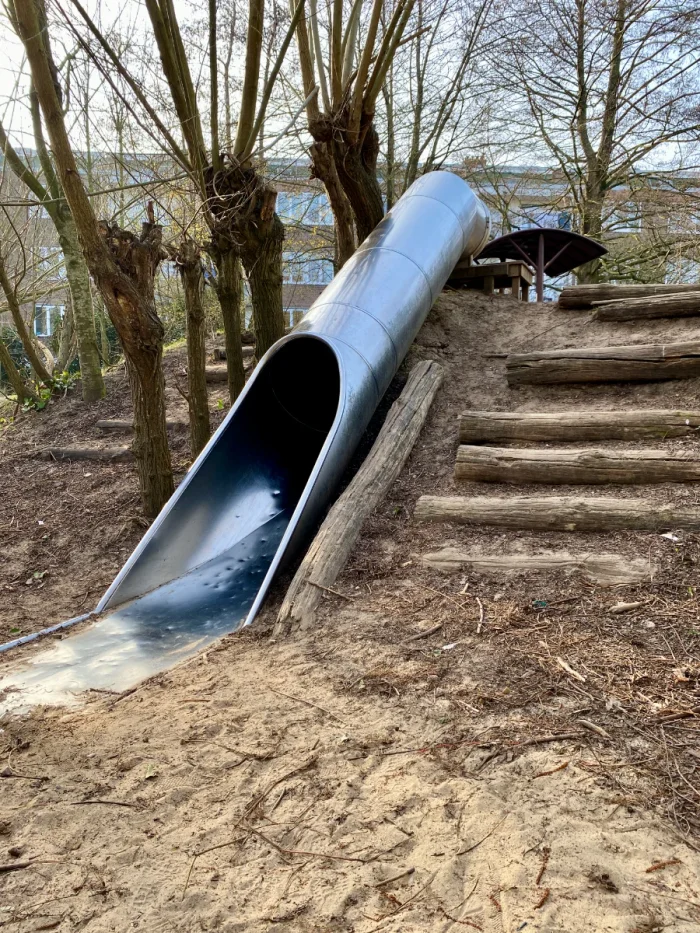 Metal slide set into a hillside with logs forming stairs to either side