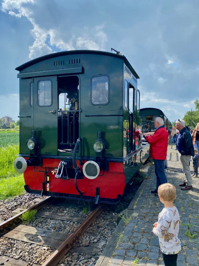 People admiring a hunter green and red historic steam train engine as it sits still at a station