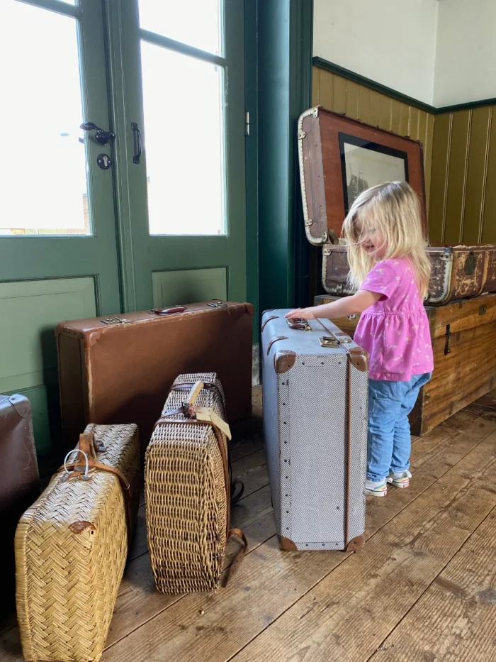 Girl plays with vintage luggage in a recreation of a train station waiting room