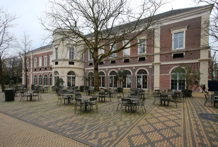 Exterior of large two story brick building with tables and chairs outside and winter tree