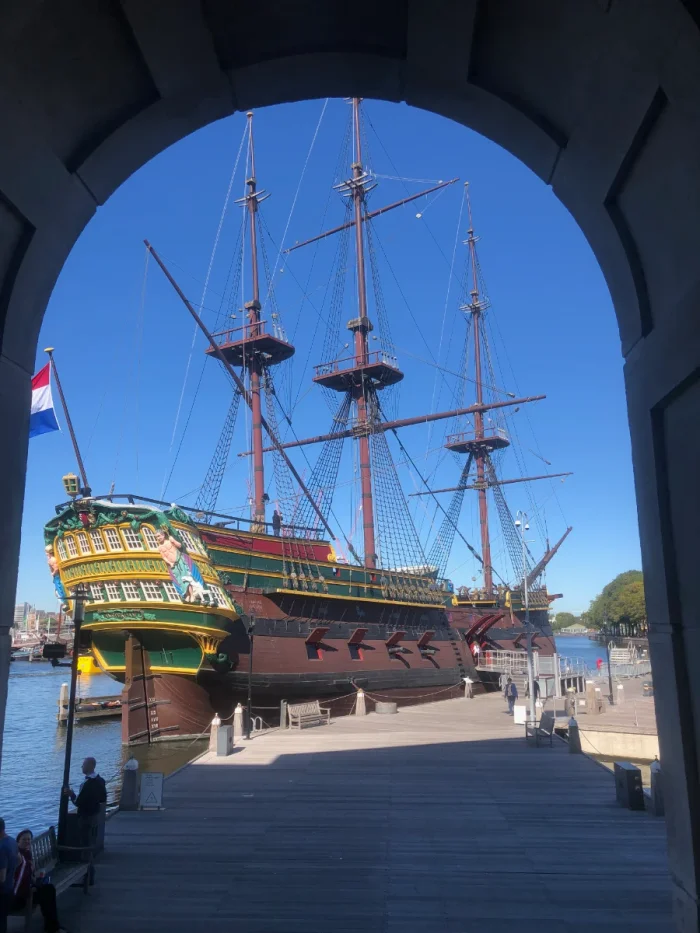 Full-size replica VOC sailing ship painted red, green, and yellow with Dutch flag on the back