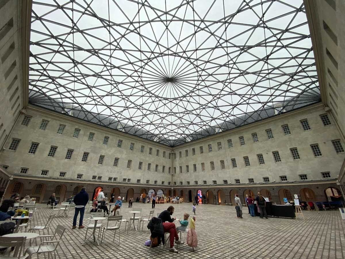 People sitting and dining in a large interior courtyard of a historic building that's covered with an intricate glass ceiling