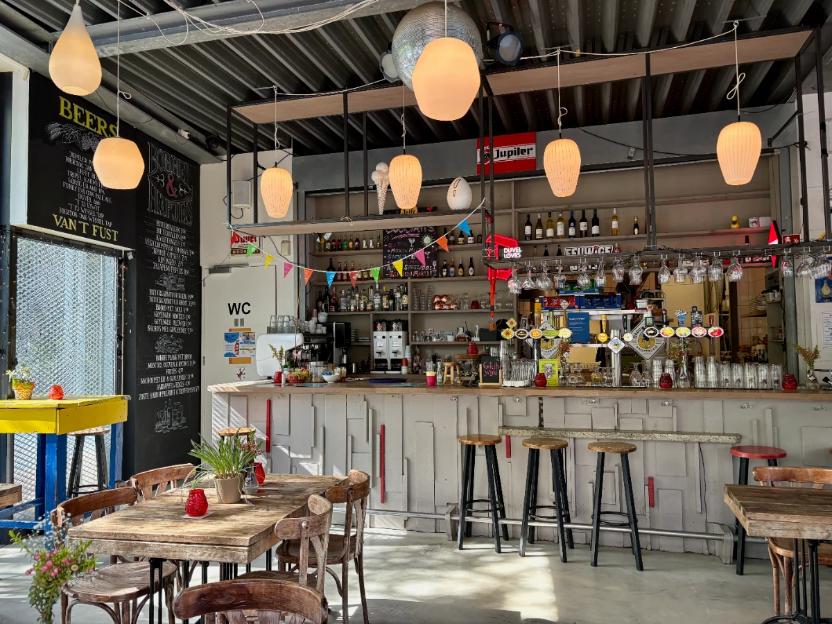 Eclectic cafe interior with wooden table and chairs, wooden bar with beer taps and wall of bottles and round globe lights overhead