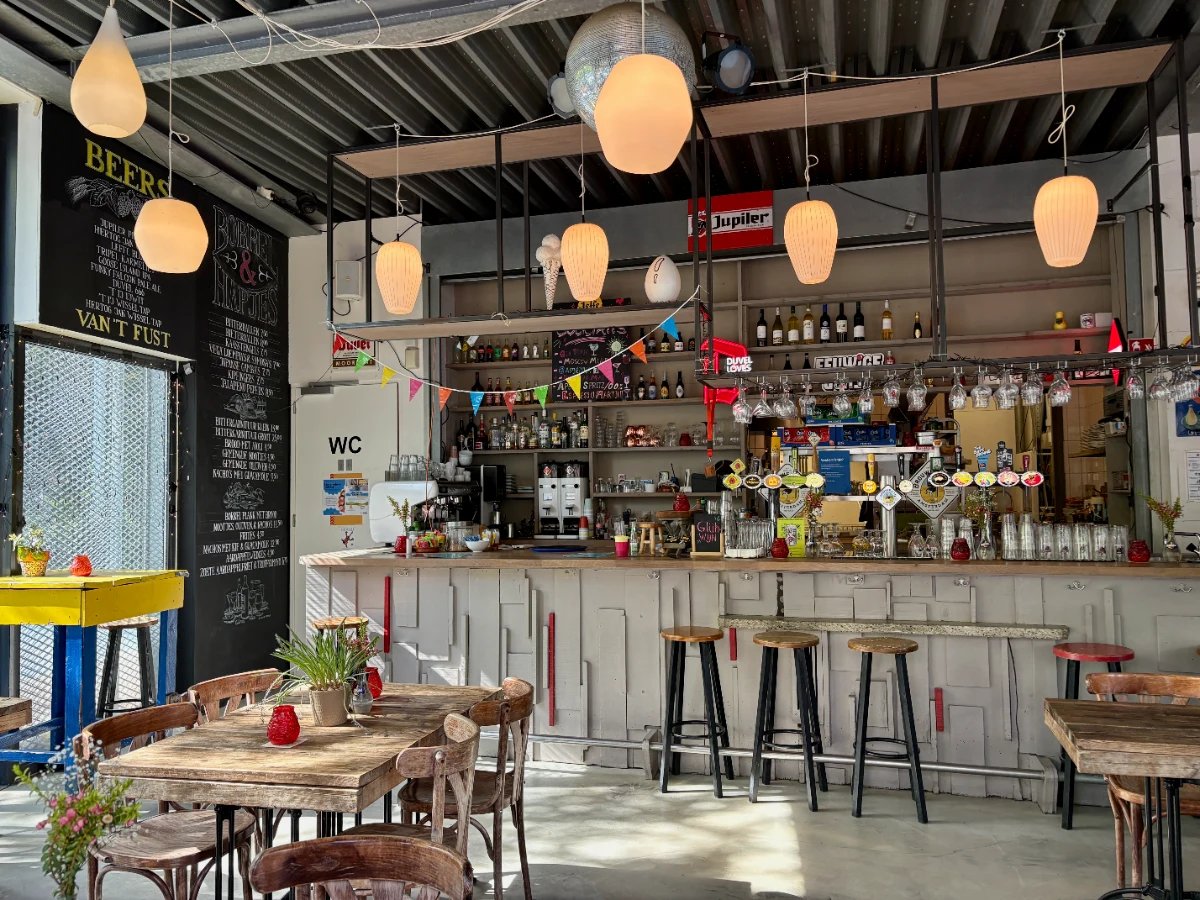 Eclectic cafe interior with wooden table and chairs, wooden bar with beer taps and wall of bottles and round globe lights overhead