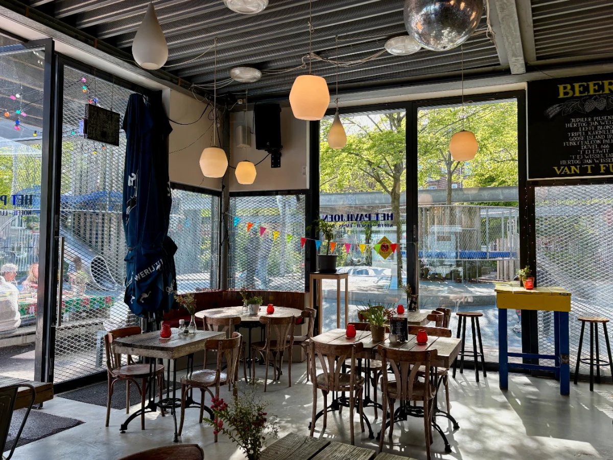 Cafe interior with wooden table and chairs and large windows looking out onto a playground