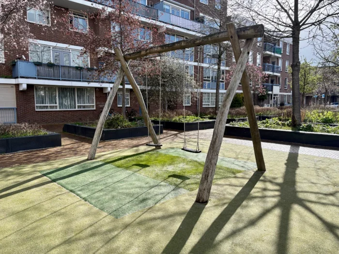 Two swings on wooden frame with residential buildings behind