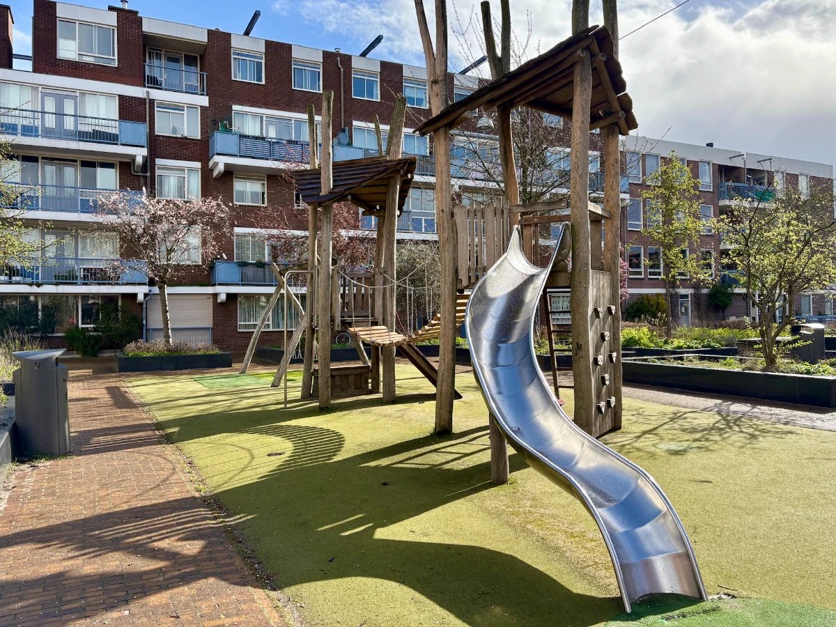 Wooden climbing structure with bridge connecting two towers and curvy metal slide
