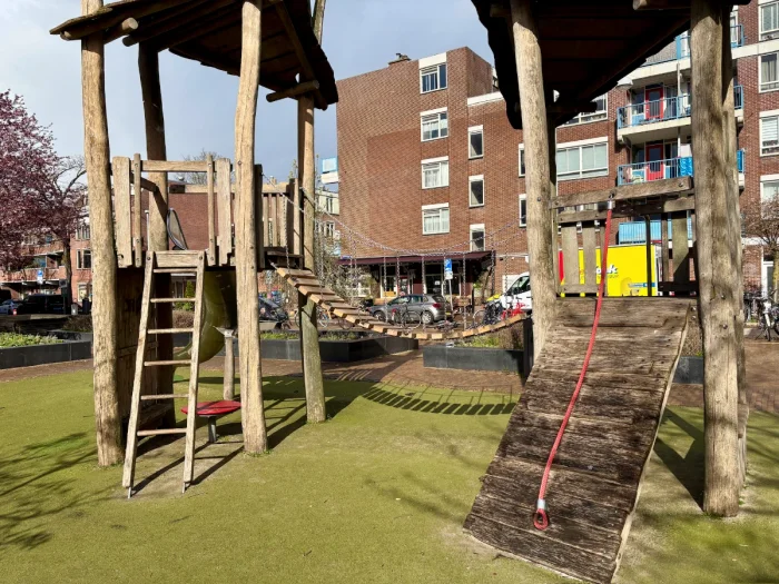 Wooden playground structure with two towers connected by a bridge and ladders and rope pull