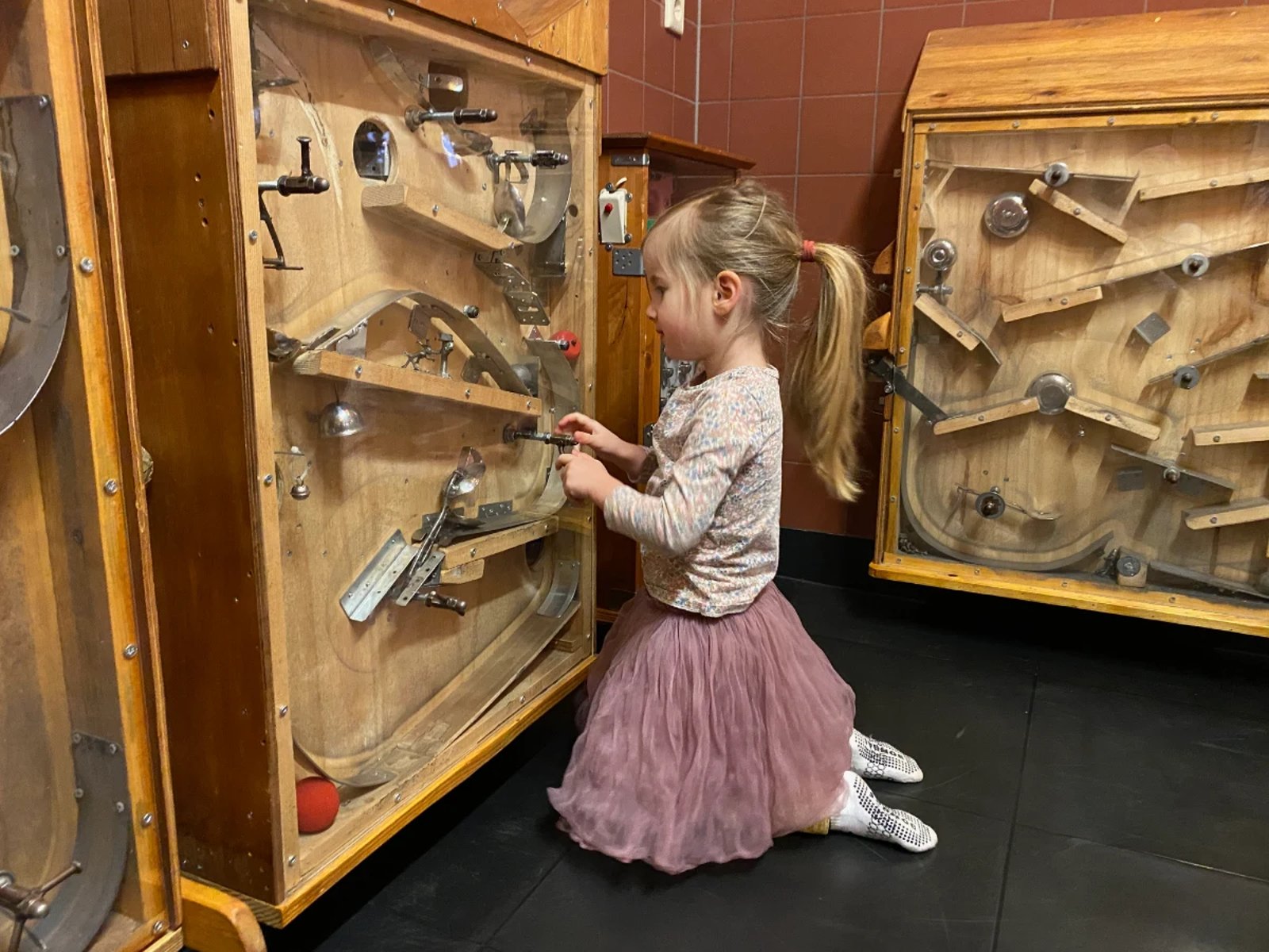 Girl playing with handmade pinball machine made out of found and recycled objects