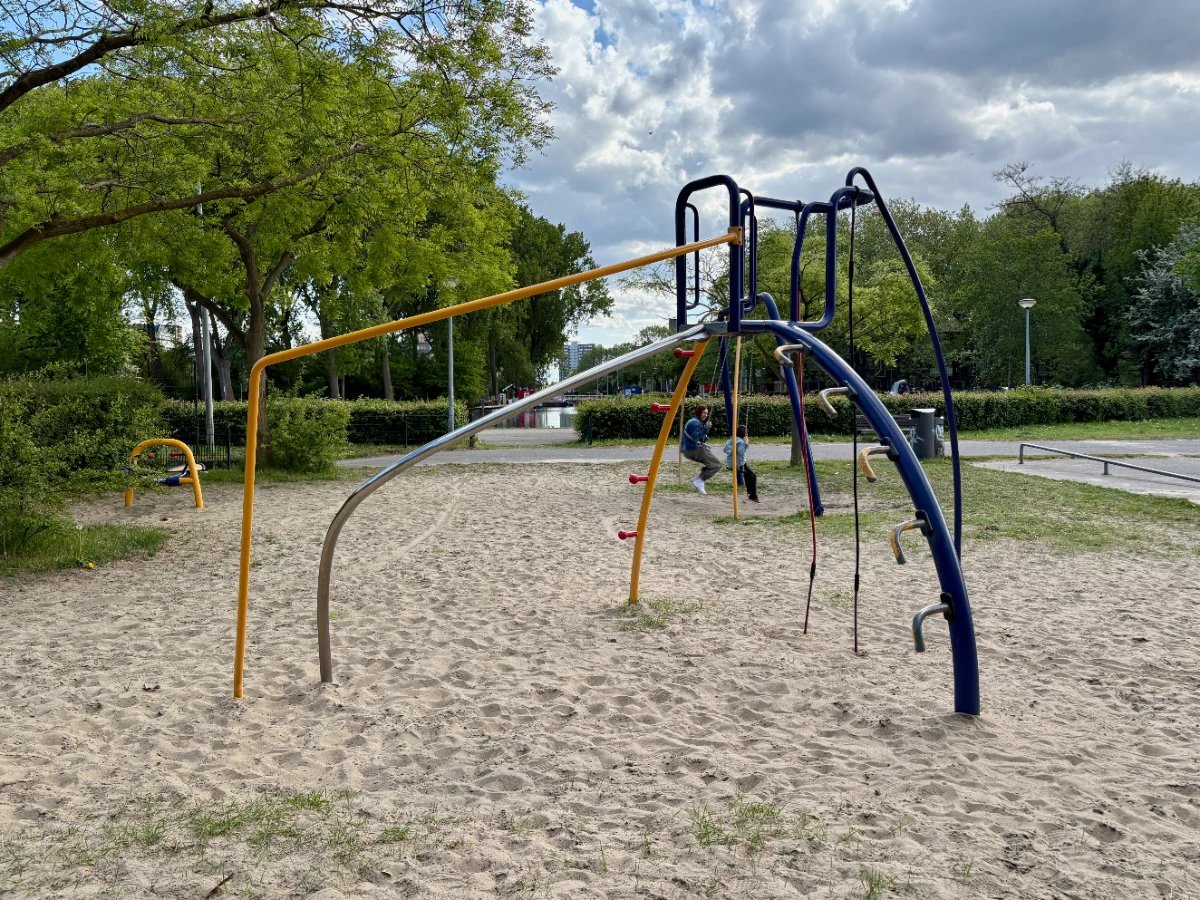 Blue and yellow modern climbing frame with mom and kid swinging behind