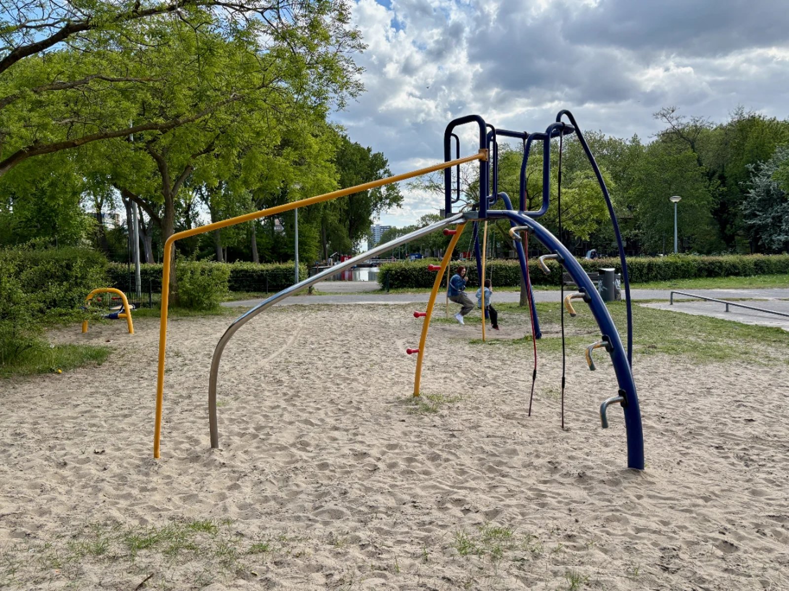 Blue and yellow modern climbing frame with mom and kid swinging behind