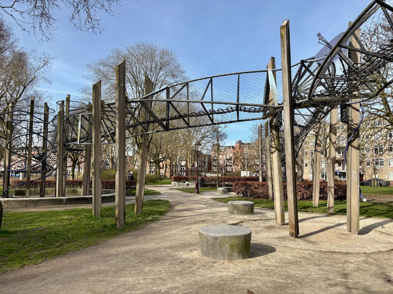 Tall wooden poles support a twisting metal, mesh, and rope walkway that stands over a park lawn