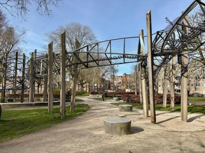 Tall wooden poles support a twisting metal, mesh, and rope walkway that stands over a park lawn