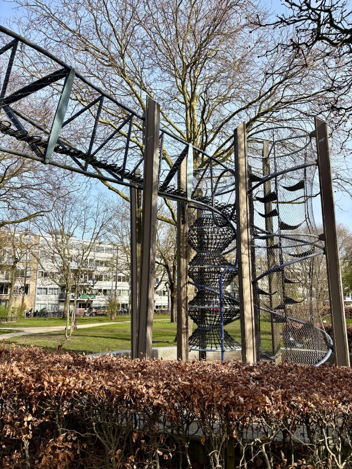 A tall triangulated metal frame surrounds a rope obstacle course with hammocks and climbing nets connecting it ot he ground and a tall winter tree behind it