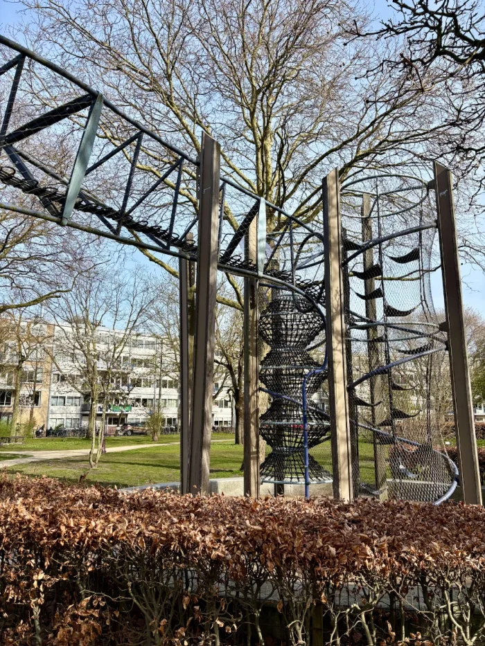 A tall triangulated metal frame surrounds a rope obstacle course with hammocks and climbing nets connecting it ot he ground and a tall winter tree behind it