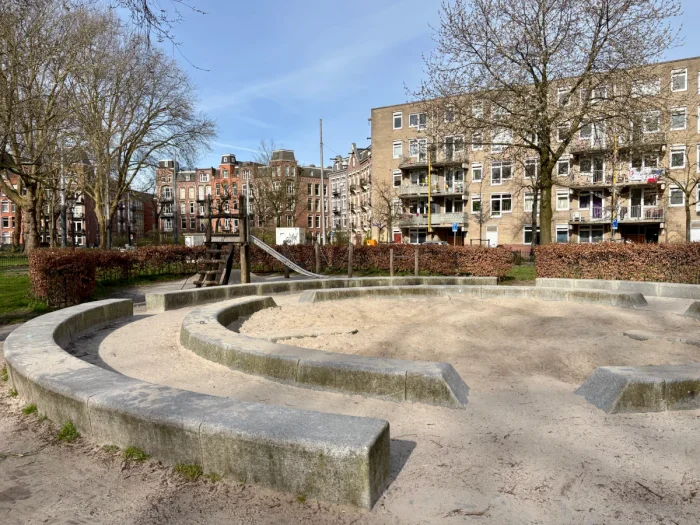 Large round sand pit with concrete edge and centric rings with residential buildings and winter trees beyond 