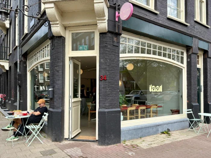 Corner coffee shop in black brick building with large white-framed windows and a man enjoying coffee outside