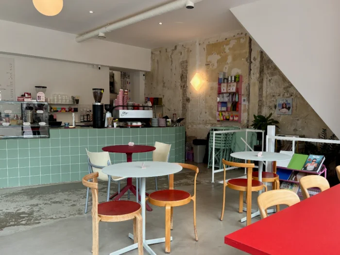 Coffeeshop interior with teal tiled bar, round white tables, and large red table
