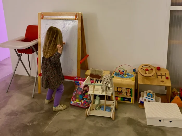 Girl coloring on a white board with high chair and other toys around
