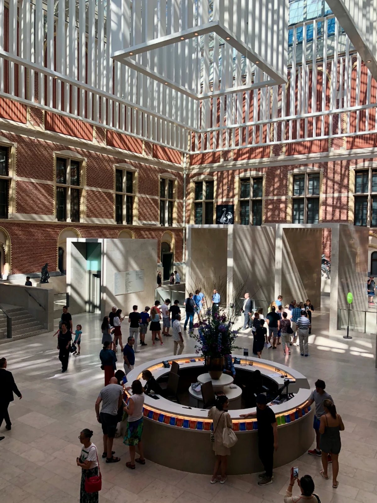 Interior courtyard of Rijksmuseum with round information desk and white modern rectangular sculpture hanging from the glass ceiling