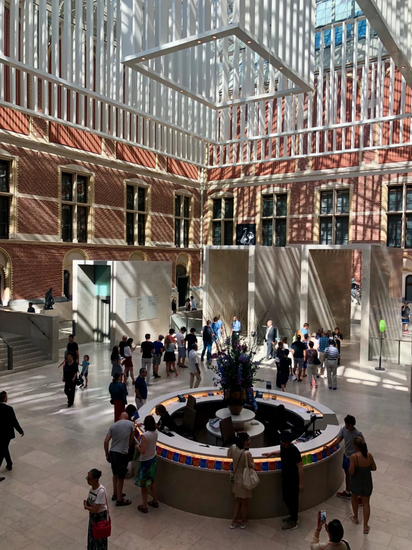 Interior courtyard of Rijksmuseum with round information desk and white modern rectangular sculpture hanging from the glass ceiling