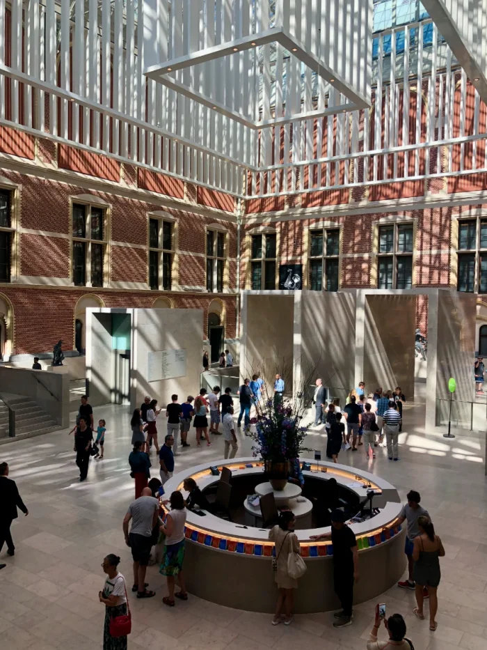 Interior courtyard of Rijksmuseum with round information desk and white modern rectangular sculpture hanging from the glass ceiling