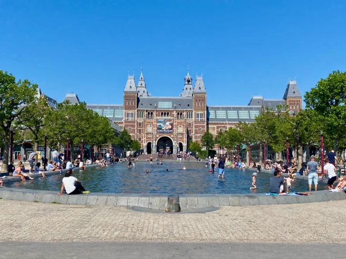 Historic Rijksmuseum building on a summer day with children playing in and parents relaxing beside a large paddling pool