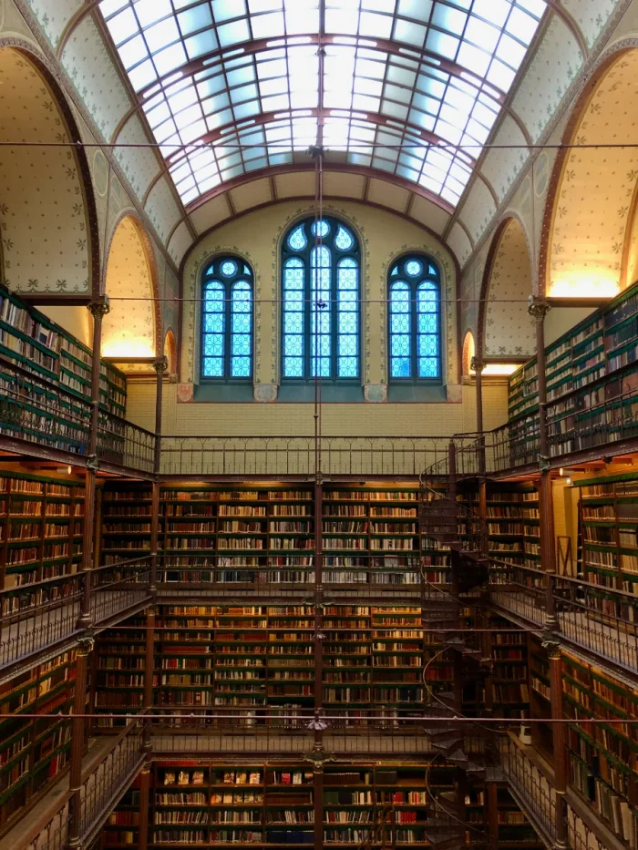 Multi-level historic library with walls lines with books, glass barrel ceiling, and spiral staircase