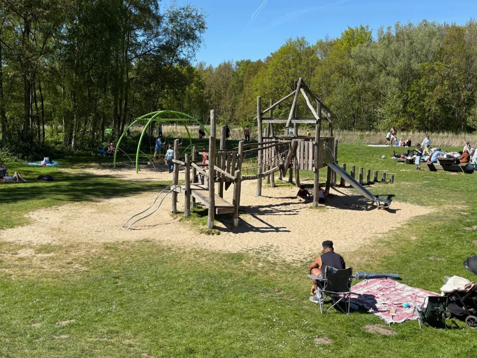Kids and parents playing and resting in the sun next to wooden playground