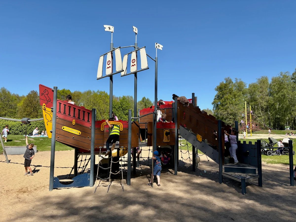 Kids playing on a pirate-themed play structure resembling a pirate ship with tall masts