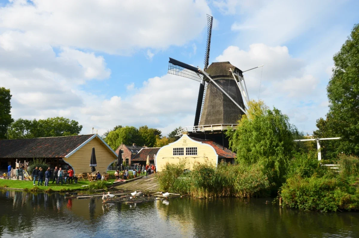 People standing outside a Dutch windmill with yellow outbuildings along a canal