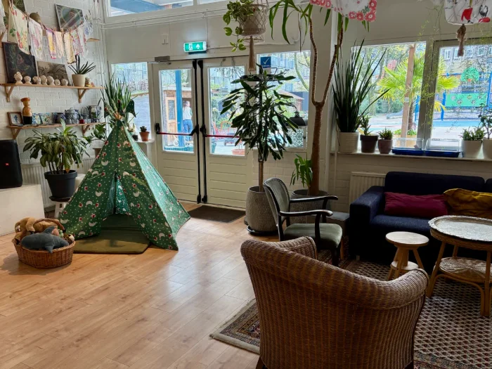 Cozy living-room-like interior of a cafe and community center with green children's teepee and windows onto playground